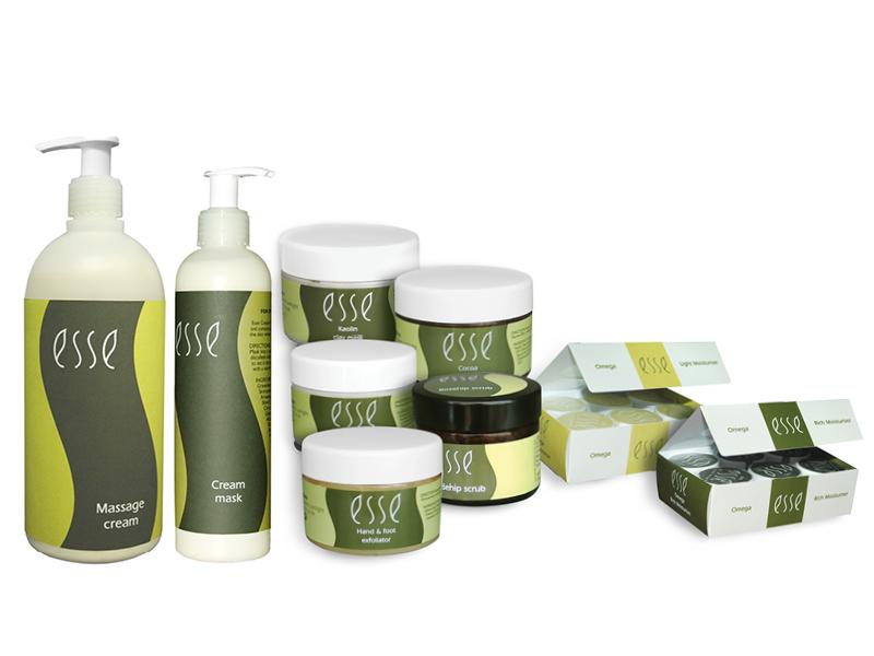 Image of various skincare products from the brand "Esse" arranged in a group. The items include bottles of massage cream and cream mask with pump dispensers, several jars of creams and scrubs with white lids, and boxes of assorted sachets labeled "Omega.