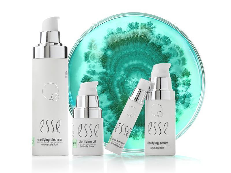 Four Esse skincare products are arranged in front of a decorative green and teal circular background. The products include a clarifying cleanser, clarifying oil, clarifying serum, and another clarifying skincare item, all in sleek white and silver packaging.
