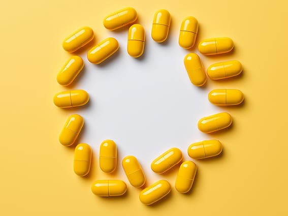 A circle made up of yellow capsules on a yellow background with a white center. The capsules are evenly spaced, creating a ring around the central empty space.