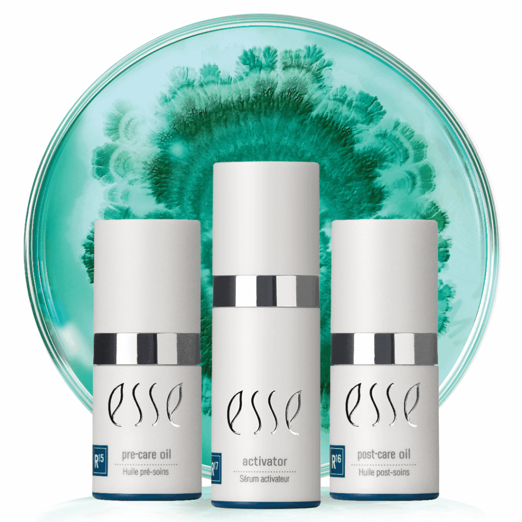 Three Esse skincare products (pre-care oil, activator, and post-care oil) are arranged in front of a round dish with a green and teal abstract pattern resembling a petri dish or watercolor art.