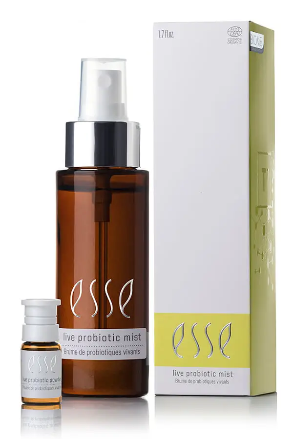 A brown spray bottle labeled "Esse live probiotic mist" stands next to its white and yellow box, with a small vial placed in front. The packaging highlights a skincare product.