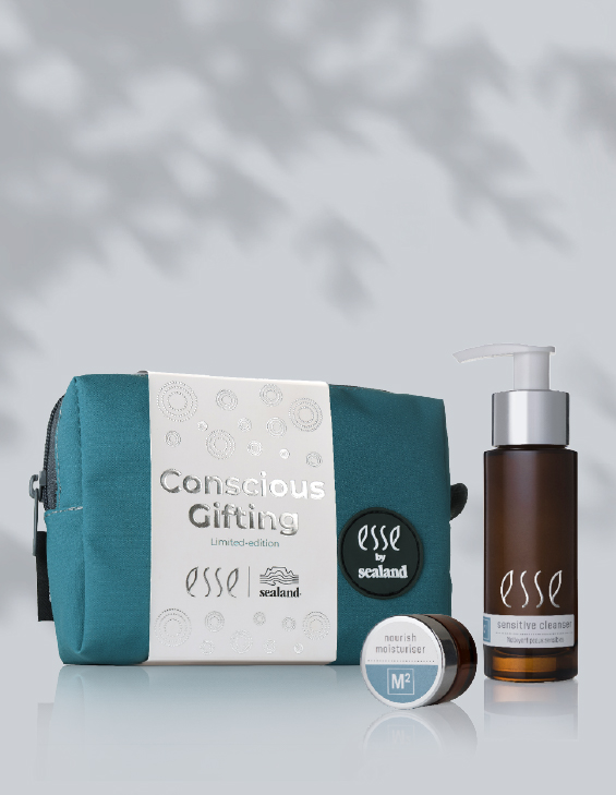 The Esse Conscious Gifting set, featuring a teal toiletry bag, nourish moisturizer jar, and pump bottle of sensitive cleanser, is displayed together on a light surface with soft shadows in the background.